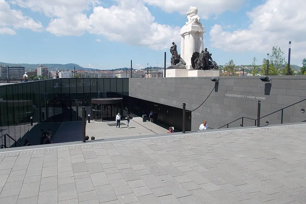 The underground Visitor Centre entrance on Kossuth Square, a glass revolving door below the level of the square, with a monument above and a sign reading látogatóközpont / visitor center